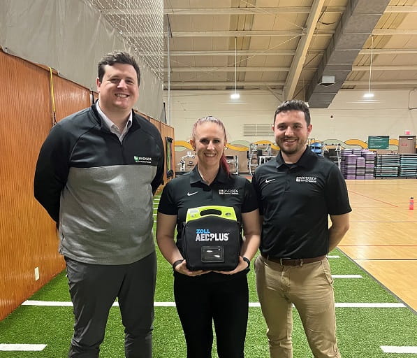 group of three athletic trainers with an AED device