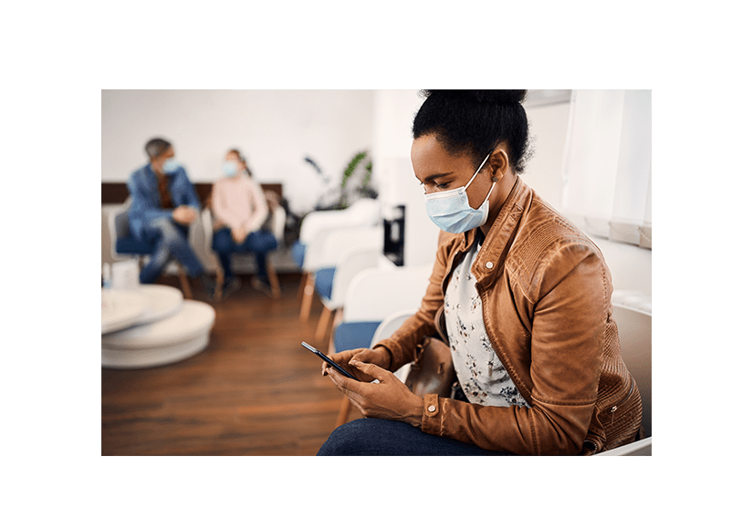 Black woman with woman face mask texting on cell phone in waiting room at medical clinic