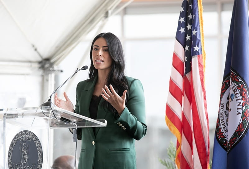 brunette woman in green suit speaking into microphone in front of american flag