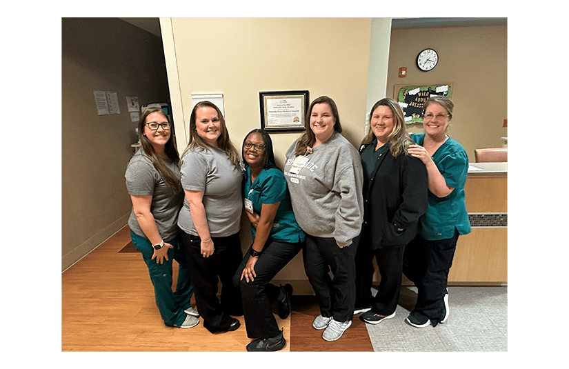 Group of nurses next to safe sleep certification on the wall