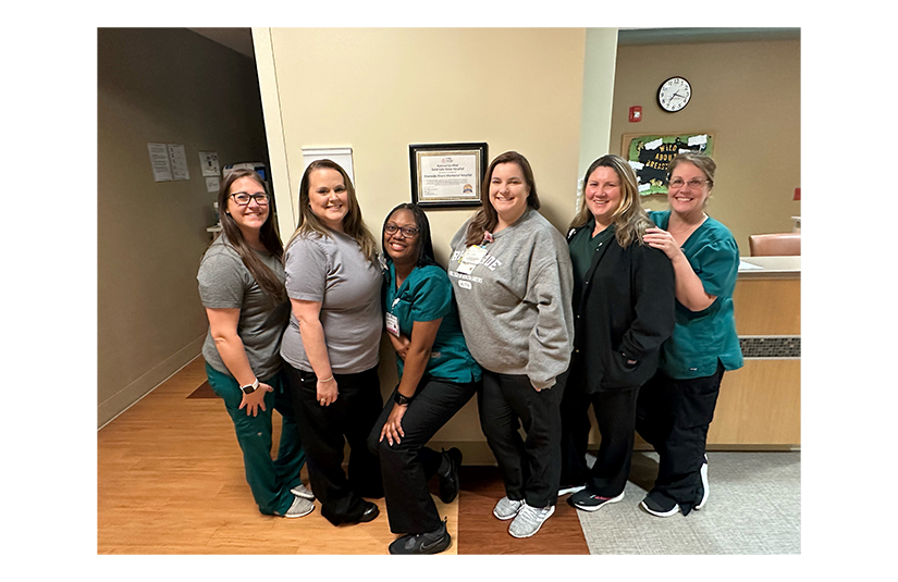 Group of nurses next to safe sleep certification on the wall