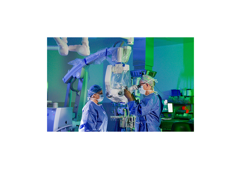 two medical professionals in surgical suite in blue scrubs with technology around them