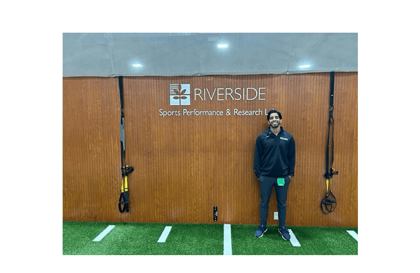 Alvin Varghese standing in front of riverside sports lab sign
