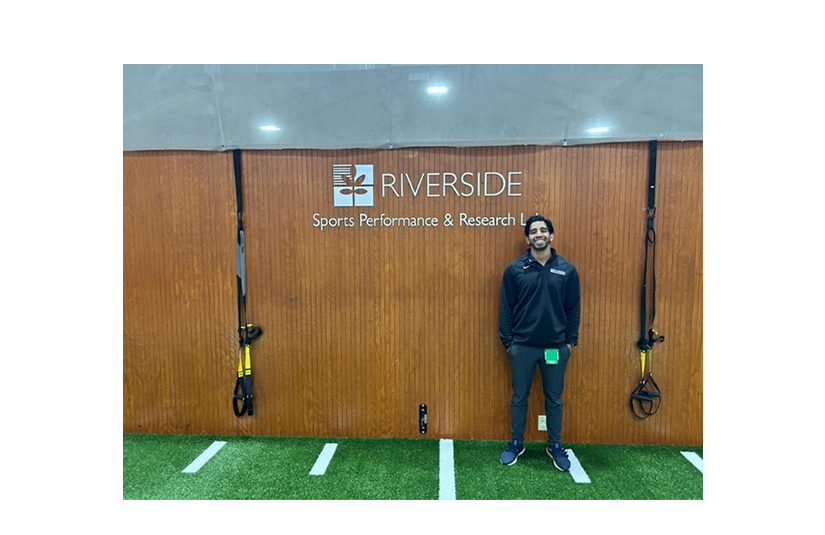 Alvin Varghese standing in front of riverside sports lab sign