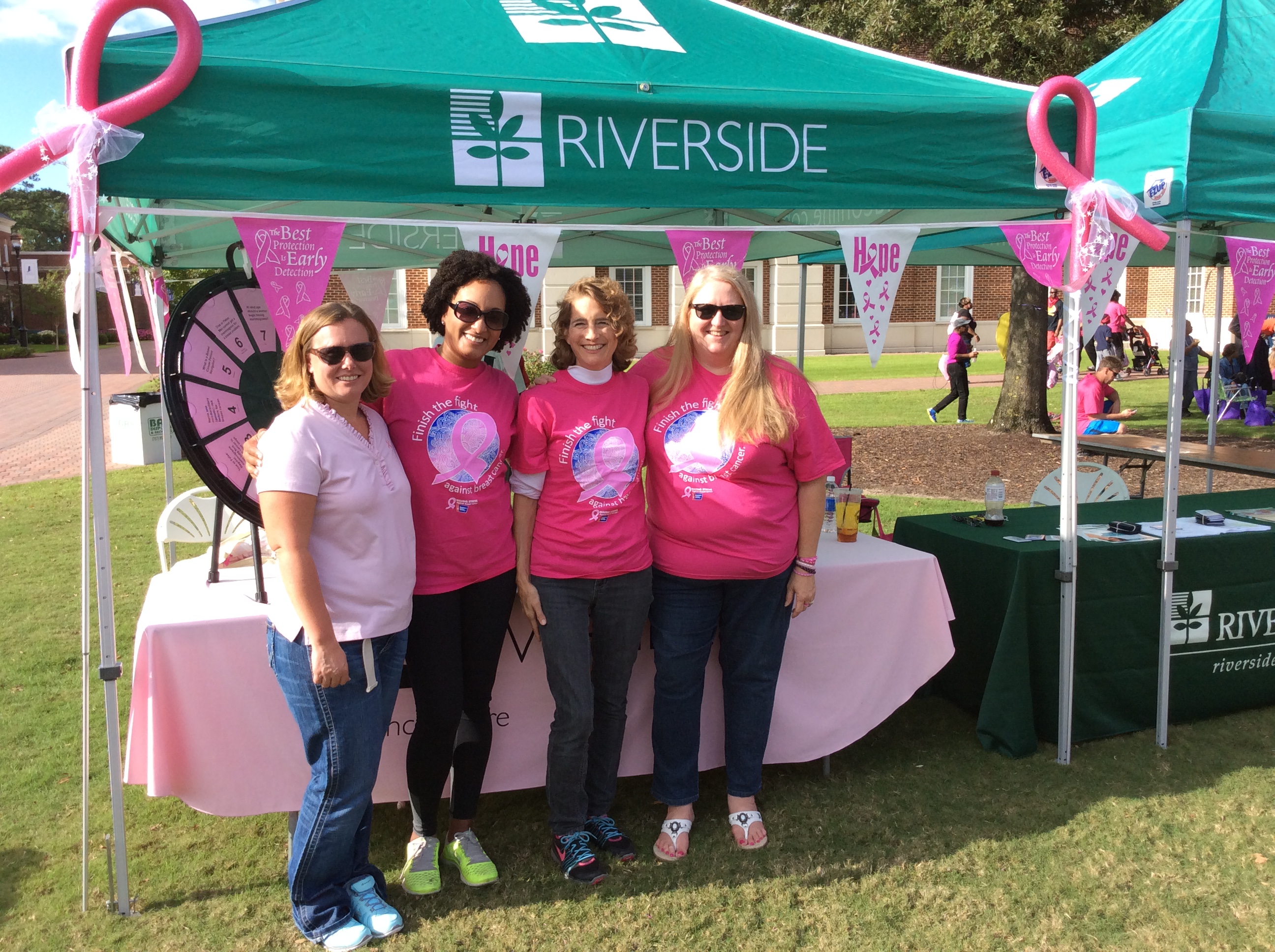 four women in pink shirts standing in front of riverside green tent