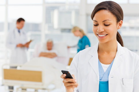 Advanced Practice Provider (APP) Fellowship Smiling young female doctor holding cellphone with colleagues and patient in background