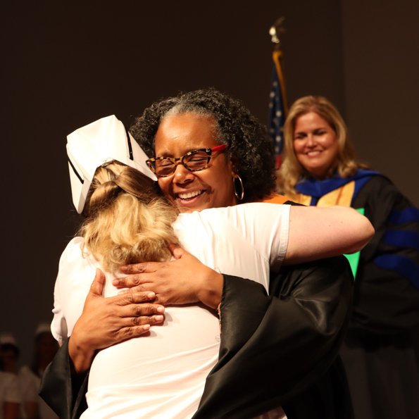female faculty member smiling and hugging a graduate