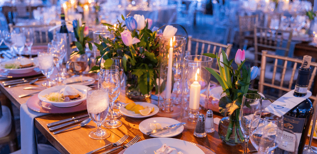 Elegant dinner table set for a formal event, featuring lit candles, wine glasses, plates with appetizers, and colorful tulip flower arrangements.
