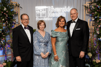 Four people in formal attire pose smiling at a Riverside Health Foundation event. The backdrop is elegantly decorated with lush greenery and flowers.