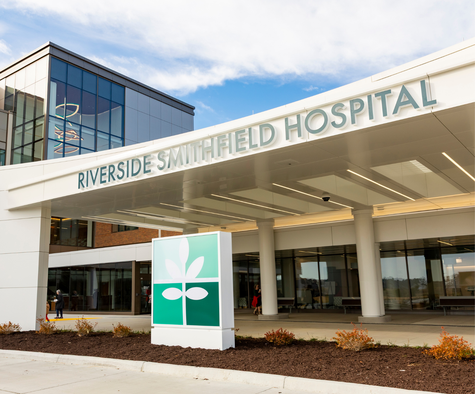 Modern hospital entrance labeled "Riverside Sandfield Hospital," featuring a sleek design with glass windows and a welcoming sign under a clear sky.