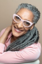 African American Woman wearing a pink shirt, and pink glasses with gray hair