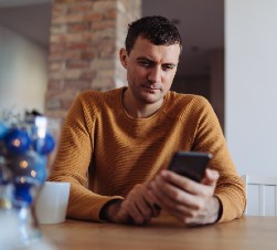 man in an orange shirt sitting at a table looking at his phone