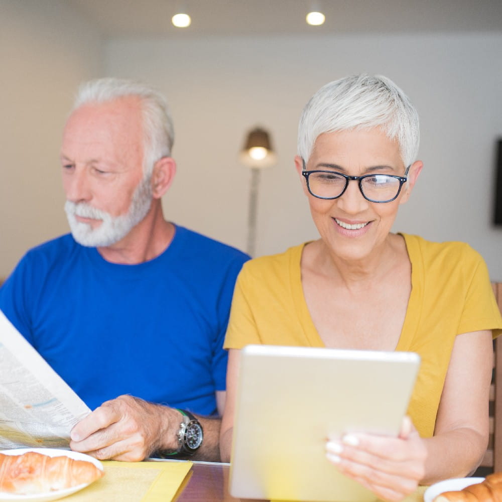 ChooseHome Members Dorvie Newsletter Smiling woman looking at digital tablet and her husband reading newspapers 