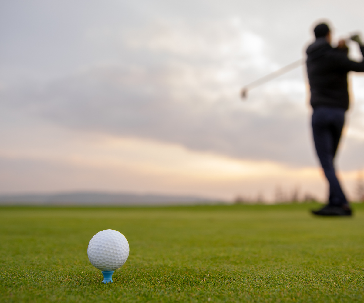 Golf ball in the forefront of the image with a man swinging a club in the background