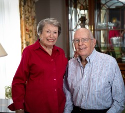 older white woman in red shirt standing next to husband in blue shirt
