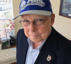 Older Caucasian Man in a black suit and a blue hat with "Air Force Falcons" printed on the hat