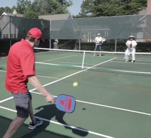 Man in red shirt playing pickleball on a green court with two others in white