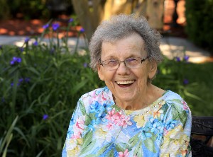 Older White woman in a colorful floral shirt smiling at the camera