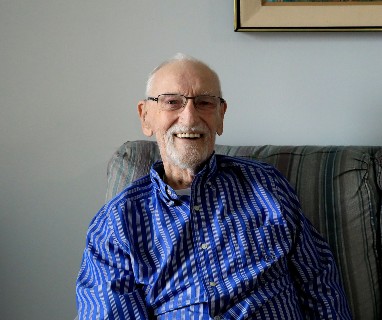 Older white man in a striped blue shirt sitting on a green couch