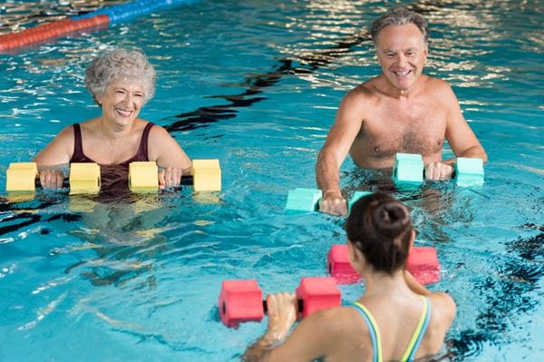 Senior couple in training session of aqua aerobics using dumbbells in swimming pool