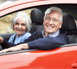 older couple smiling sitting in a red car