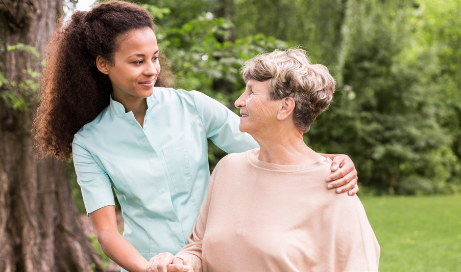 Memory Care Navigation African American Woman smiling at an older White woman in a peach shirt