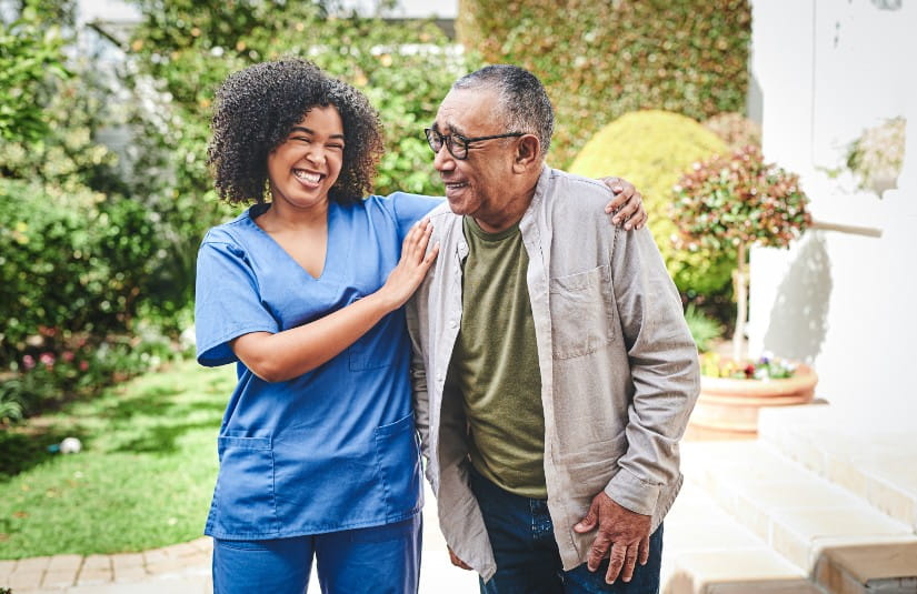 Healthcare professional walking alongside an older adult on a garden pathway outside a residential community, demonstrating compassionate assisted living support, senior care services and personalized daily assistance.