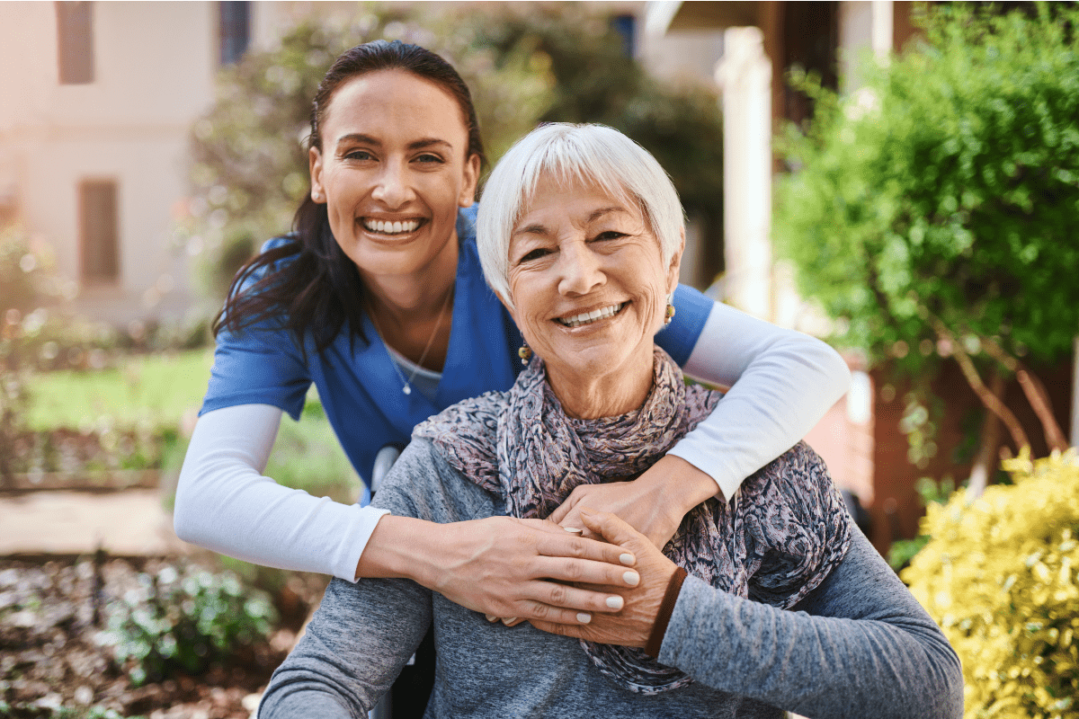 Caregiver embracing an older adult outdoors at an assisted living community, highlighting compassionate senior care, personalized support, wellness services and a welcoming senior living environment.