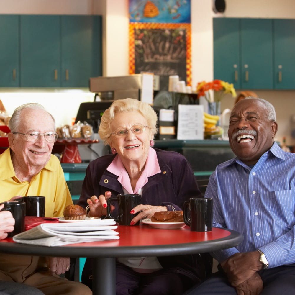 Older adults enjoying coffee and conversation in a senior living community dining area, highlighting social engagement, wellness programs, community amenities and an active retirement lifestyle.