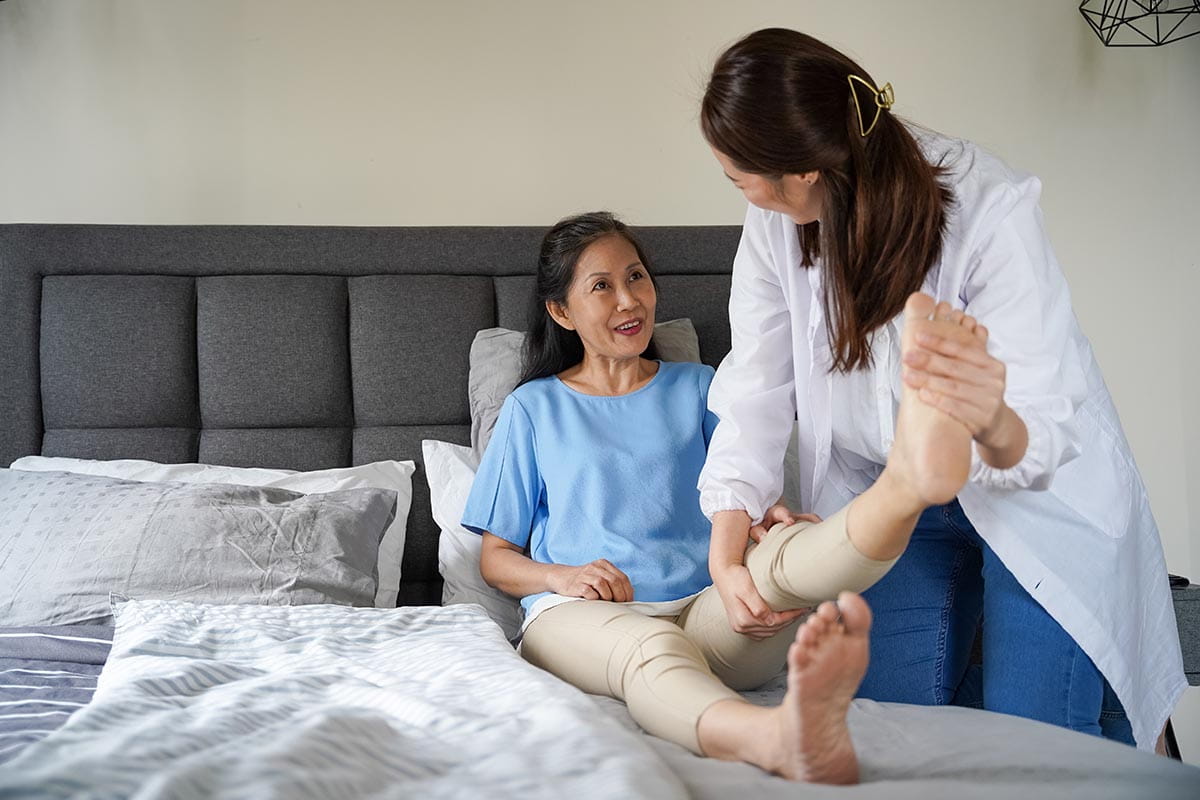 An Asian woman doing physical exercises with her therapist at home.