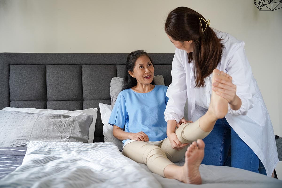 An Asian woman doing physical exercises with her therapist at home.