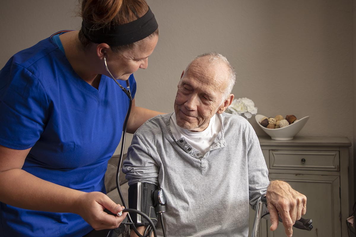 A female nurse caring for an elderly man at his home.