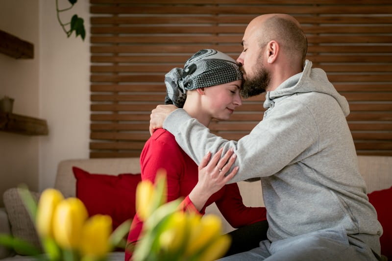 Man and woman embracing. Man kissing Cancer patient on the forehead