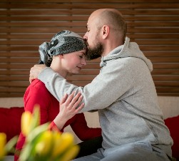 Man and woman embracing. Man kisses cancer survivor on the forehead.