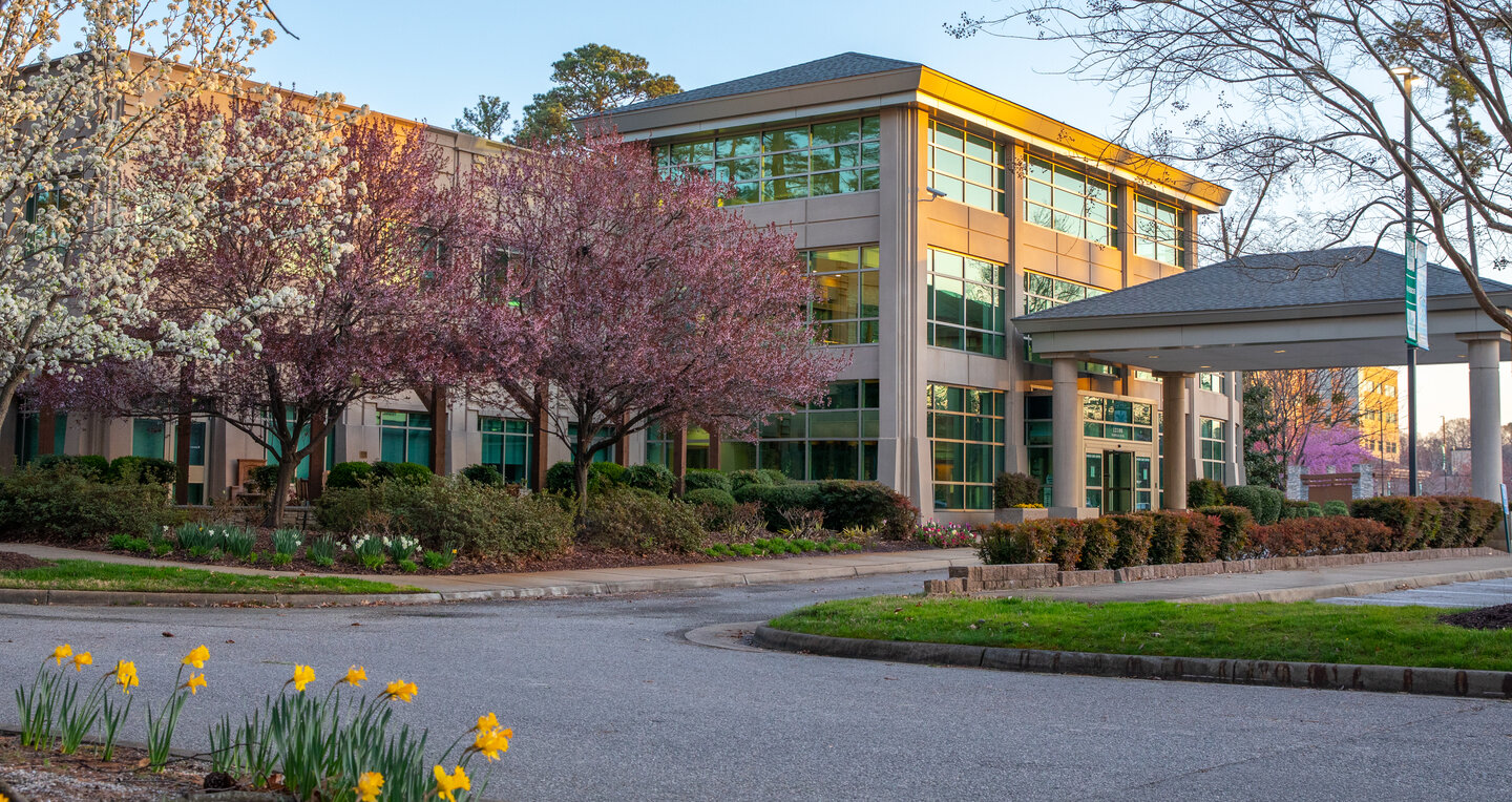 Radiation Oncology Specialists Newport News with large glass windows is surrounded by blooming pink and white trees and vibrant yellow daffodils in spring.