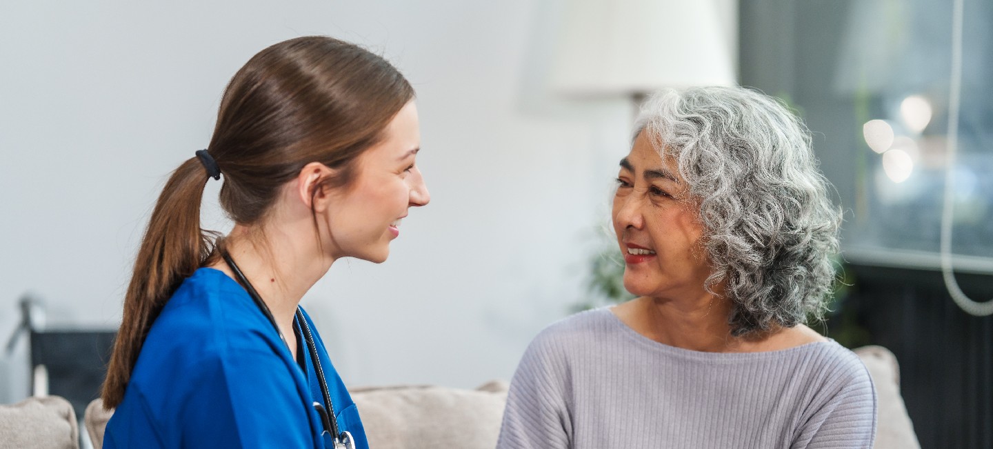 Caucasian female doctor offers encouragement to Asian mature elderly patient woman while holding hands, providing comfort and support during a medical consultation at sofa