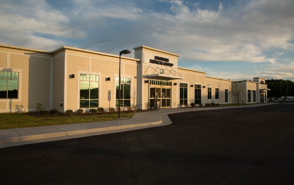 A modern beige commercial building under a partly cloudy sky, featuring large windows and a reflective entrance. The mood is calm and businesslike.