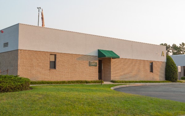 Single-story brick building with a flat roof and a green awning over the entrance. The grass lawn is well-maintained, giving a neat, professional tone.