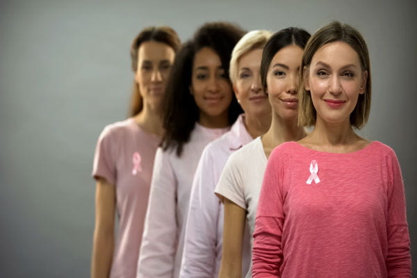 Happy women wearing pink shirts and breast cancer ribbons, standing in line
