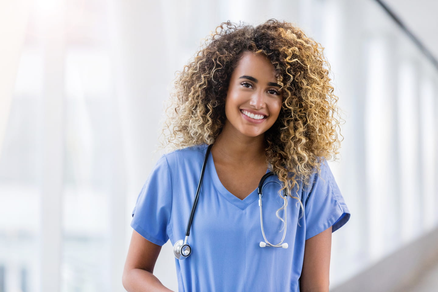 Beautiful young adult female healthcare professional stands in a hospital hallway. She is smiling at the camera.