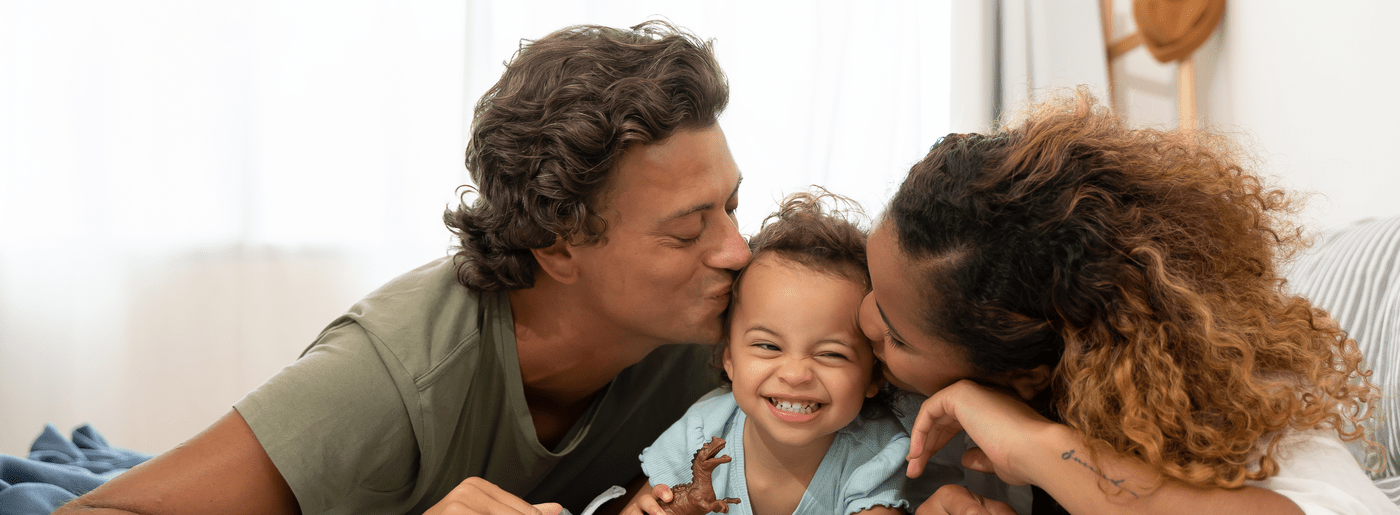 Conquering cancer means everything to us. Mixed races family Father mother kiss daughter, aged three and hugging together on a bed. Activity wellness happy at home.