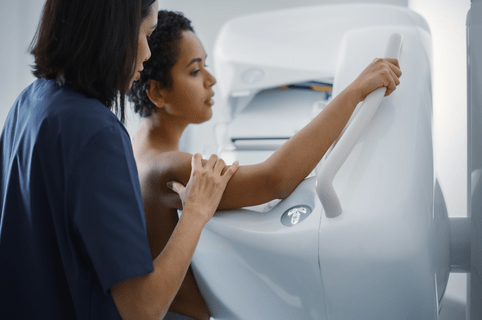 Friendly Female Doctor Explains the Mammogram Procedure to a Topless Latin Female Patient with Curly Hair Undergoing Mammography Scan. Healthy Female Does Cancer Prevention Routine in Hospital Room.