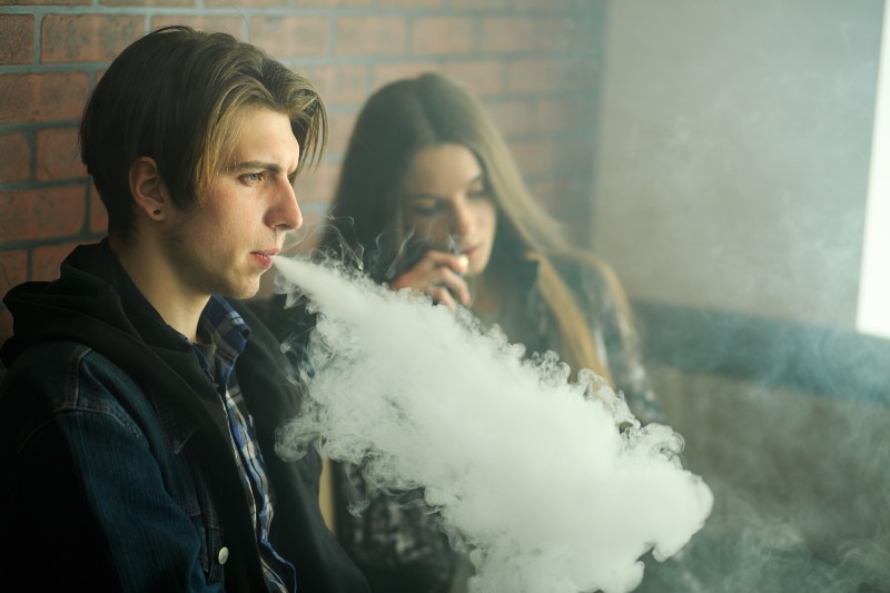 girl in sunglasses and young guy smoke an electronic cigarette