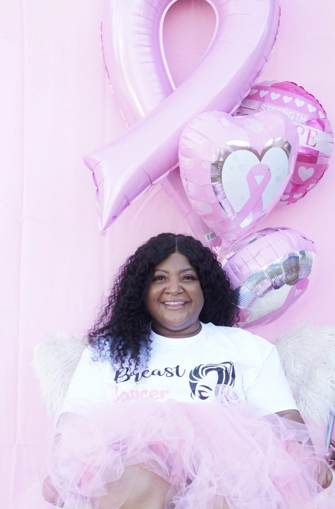 African American Woman smiling siting in front of a pink wall 