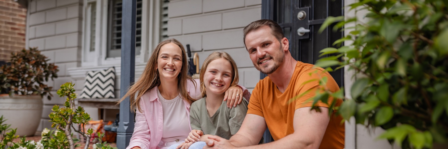 Smiling family seated before entrance of their house