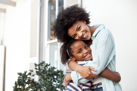 Portrait of a cheerful mother and daughter giving each other a hug while looking at the camera outside during the day