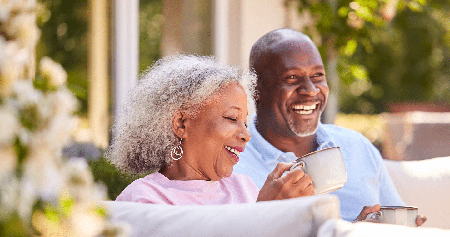 Retired Couple Sitting Outdoors At Home Having Morning Coffee Together