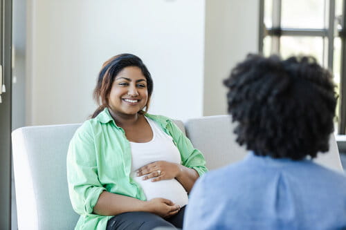 A cheerful soon-to-be new mother smiles during a session with an unrecognizable mental health professional.