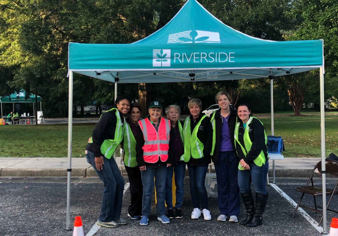 Riverside Health team members standing together under a Riverside tent at a community event.