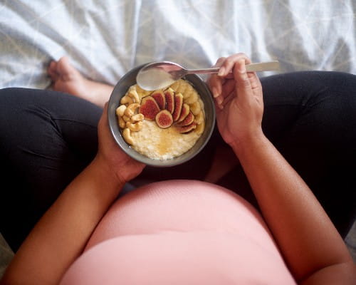 High angle shot of an unrecognizable pregnant woman having a healthy breakfast while sitting on her bed